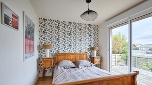 Une chambre à coucher avec un lit en bois, deux tables de chevet, une grande fenêtre et un papier peint à motifs.