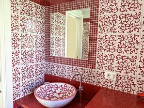 Ein Badezimmer mit einem großen, dekorativen Waschbecken, einem Spiegel und gemusterten Fliesen.