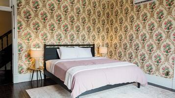 A bedroom with a bed, two bedside lamps, a patterned wallpaper, and a staircase.