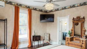 Een slaapkamer met een groot bed, een houten dressoir, een stoel, een televisie en een plafondventilator.