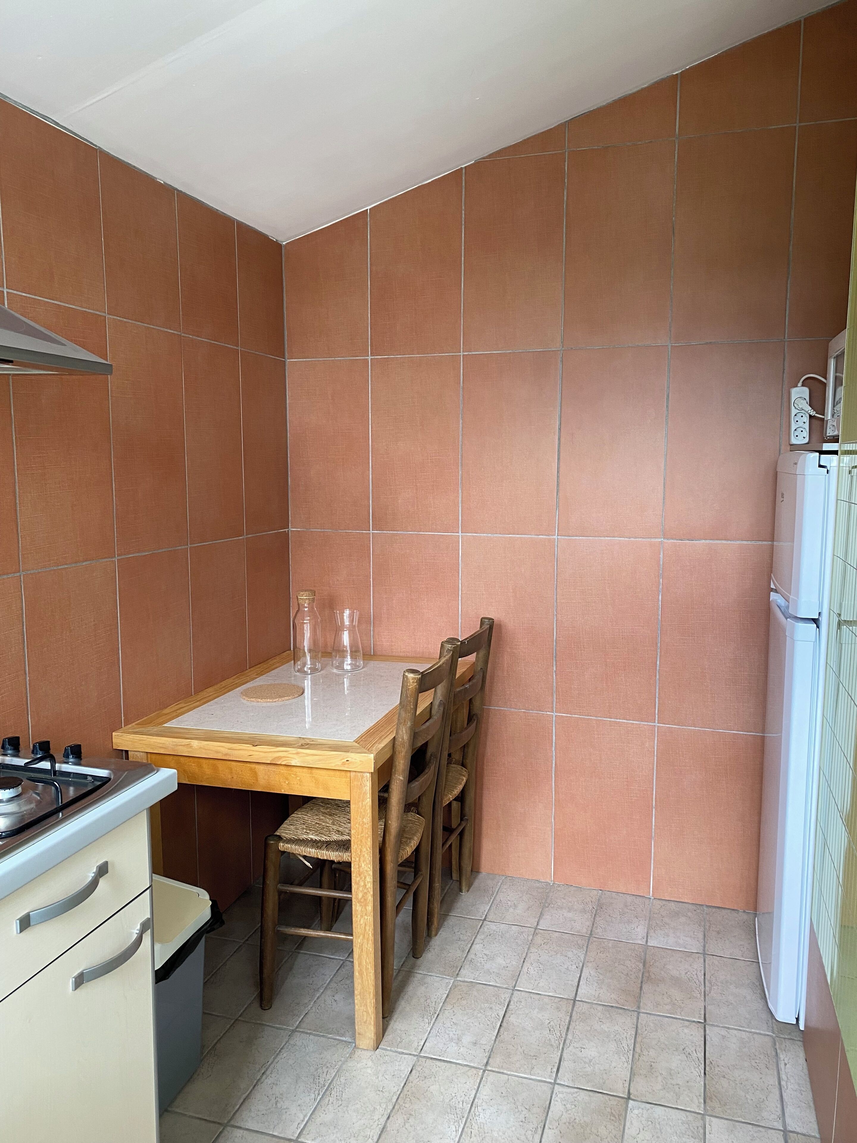 Una cucina compatta con un tavolo di legno, sedie, un fornello a gas e un frigorifero bianco.