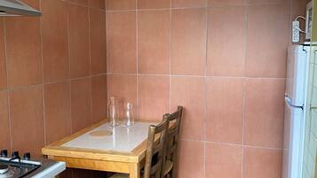Una cucina compatta con un tavolo di legno, sedie, un fornello a gas e un frigorifero bianco.