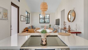 A modern kitchen with a central island, a dining area with a round table, and a living space with a sofa and chairs.