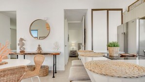 A modern kitchen with a stainless steel refrigerator, a dining area with wicker chairs and a round table, and a hallway leading to another room.
