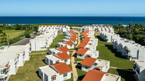 A row of white villas with red roofs, arranged in a linear fashion along a beachfront, with the ocean visible in the background.