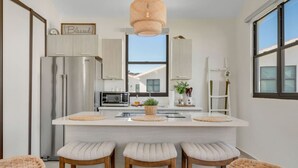 A modern kitchen with a central island, stainless steel appliances, and a view through the window.