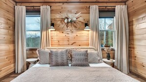 Ein Schlafzimmer einer Holzhütte mit einem Bett, zwei Nachttischen, einem Fenster mit Vorhängen und einer Wanddekoration.