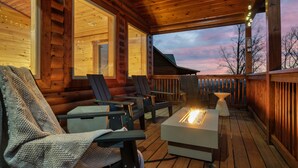 Eine Holzterrasse mit Feuerstelle und Stühlen, großen Fenstern und Blick zum Himmel.