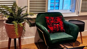 Una habitación con un sillón verde, un helecho en maceta y una ventana con persianas.