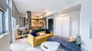 A modern living room with a yellow sofa, a grey sofa, a round coffee table, and a kitchen in the background. - Luxury Patio Suite + Pool + Gym + Lounge + Wi-Fi + Free Parking (Bellevue)