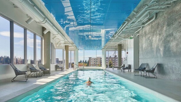 A large indoor swimming pool with clear blue water, surrounded by lounge chairs and large windows offering views of the city. - Luxury Patio Suite + Pool + Gym + Lounge + Wi-Fi + Free Parking (Bellevue)
