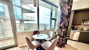 A modern kitchen with a view of the city, a round table with chairs, and a large column with a unique design. - Luxury Patio Suite + Pool + Gym + Lounge + Wi-Fi + Free Parking (Bellevue)