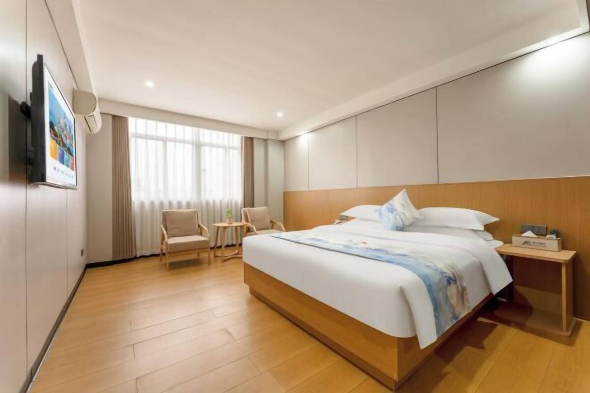 Ein modernes Hotelzimmer mit einem großen Bett, einem kleinen Schreibtisch, einem Stuhl und einem an der Wand befestigten Fernseher.