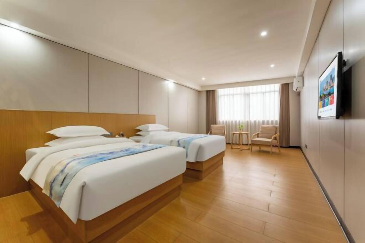Ein Hotelzimmer mit zwei Betten, einem Fernseher, einem Fenster mit Vorhängen und einem Holzboden.