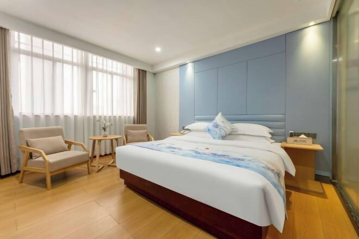 Ein Hotelzimmer mit einem großen Bett, zwei Sesseln, einem kleinen Tisch und einem Nachttisch.