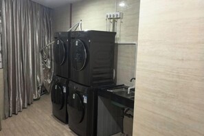 A compact hotel room with a washing machine, a small sink, and a curtain. - Charming Hotel (Heshan)