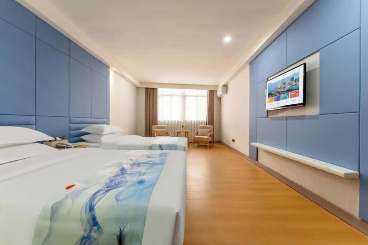 A hotel room with two beds, a TV, a window with curtains, and a wooden floor.