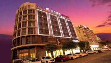 Un hotel de varios pisos con fachada curva, ventanas iluminadas y un estacionamiento con varios coches.