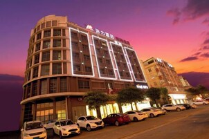 Un hotel de varios pisos con fachada curva, ventanas iluminadas y un estacionamiento con varios coches.