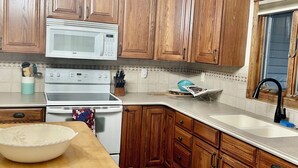 Una cocina con armarios de madera, un microondas blanco, una estufa y una mesa grande de madera.