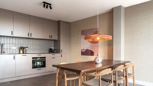 A modern kitchen with a wooden dining table and chairs, a hanging pendant light, and a tiled backsplash. - 4 Person Apartment in the City Center (The Hague)