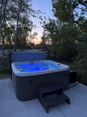 A hot tub with a bench and step, surrounded by trees and a clear sky.