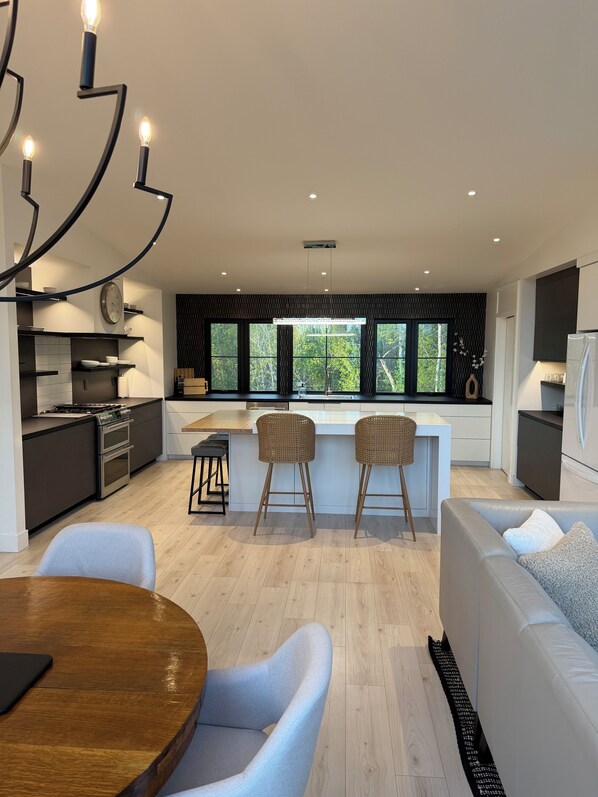 A modern kitchen with a dining area, a sofa, and a view of the outdoors.
