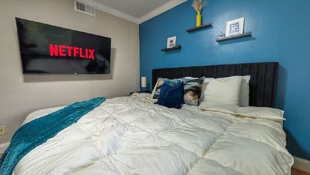 Een slaapkamer met een bed, een aan de muur bevestigde televisie en een blauwe muur.