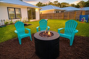 A backyard with a fire pit, two turquoise chairs, and a wooden fence.
