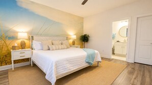 A bedroom with a bed, bedside tables, a nightstand, a lamp, a plant, and a bathroom visible through an open door. - Family Retreat - Arcade, Fire Pit, Game Room, King Bed - 2 mi Downtown! (St. Augustine)