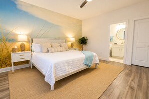 A bedroom with a bed, bedside tables, a nightstand, a lamp, a plant, and a bathroom visible through an open door. - Family Retreat - Arcade, Fire Pit, Game Room, King Bed - 2 mi Downtown! (St. Augustine)
