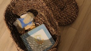 Een rieten mand met een boek en een teddybeer op een houten vloer.