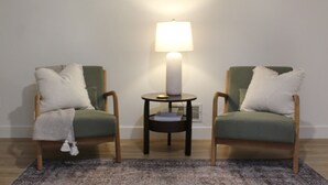 Een kamer met twee groene fauteuils, een klein rond tafeltje met een lamp en een kamerbreed tapijt met dessin.