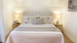 Een net opgemaakt bed met een geruit sprei, twee nachtkastjes met lampen en een schilderij aan de muur.