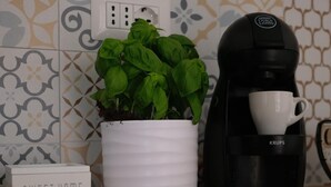 A kitchen counter with a white coffee maker, a potted basil plant, and a sign that reads "SWEET HOME".