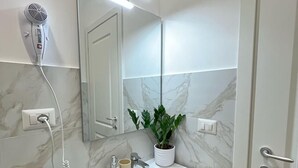 A bathroom with a white sink, a mirror, a hairdryer, and a potted plant.