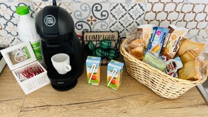 A coffee maker, a basket of bread and snacks, and a box of utensils on a wooden table.
