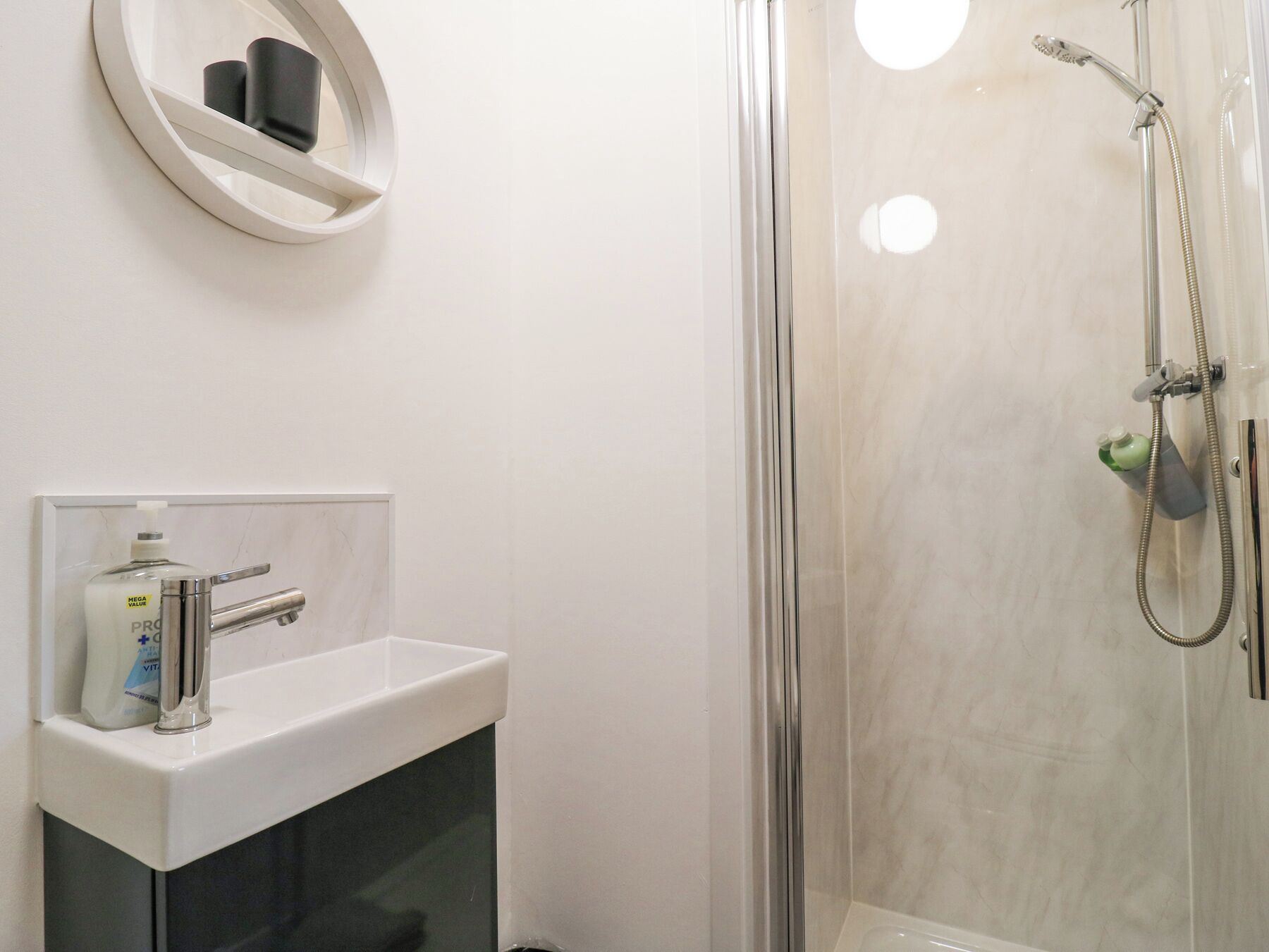 A modern bathroom with a glass-enclosed shower, a white sink with a chrome faucet, and a soap dispenser.