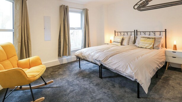 Un dormitorio moderno con cama, una mecedora, una ventana con cortinas y una lámpara de pared.