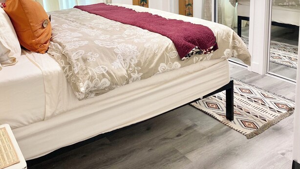 Makuuhuone, jossa on sänky, verhot, pieni pöytä, jossa on kasvi, ja kuviollinen matto.