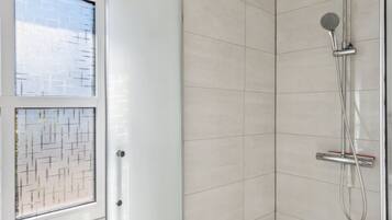 Een moderne badkamer met een glazen douchecabine, betegelde wanden en een douchekop.