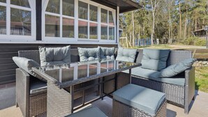 Un patio al aire libre con mobiliario de mimbre, incluyendo un sofá y una mesa con cojines.