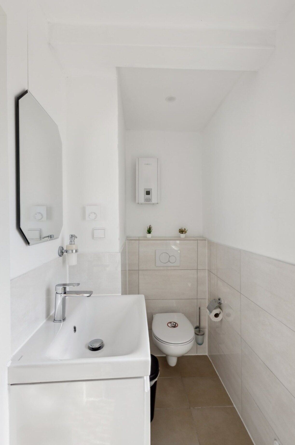 A compact bathroom with a white sink, mirror, toilet, and a small cabinet.