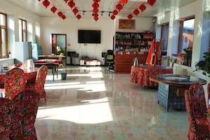 A hotel lobby with a TV, a reception desk, and a dining area with tables and chairs.