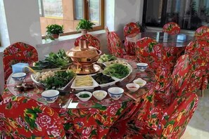 Uma mesa de jantar redonda com um pote quente central, rodeada por cadeiras estampadas com flores.