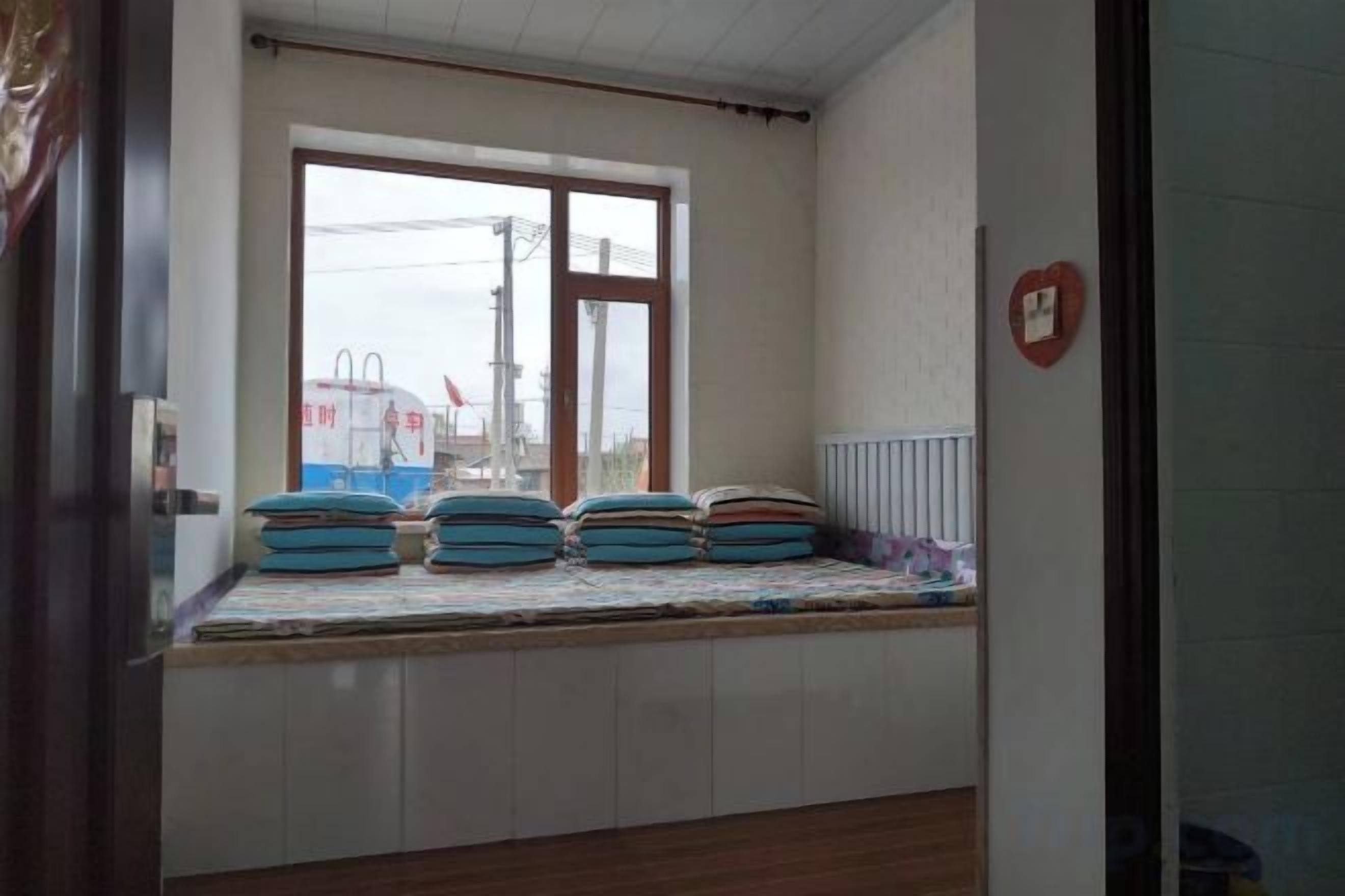 Una habitación con ventana, una cama con colchón, un radiador y una decoración con forma de corazón colgada en la pared.