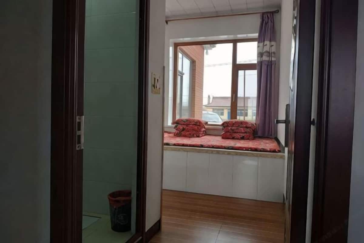 A narrow hallway leading to a room with a window seat and a view of the outside.