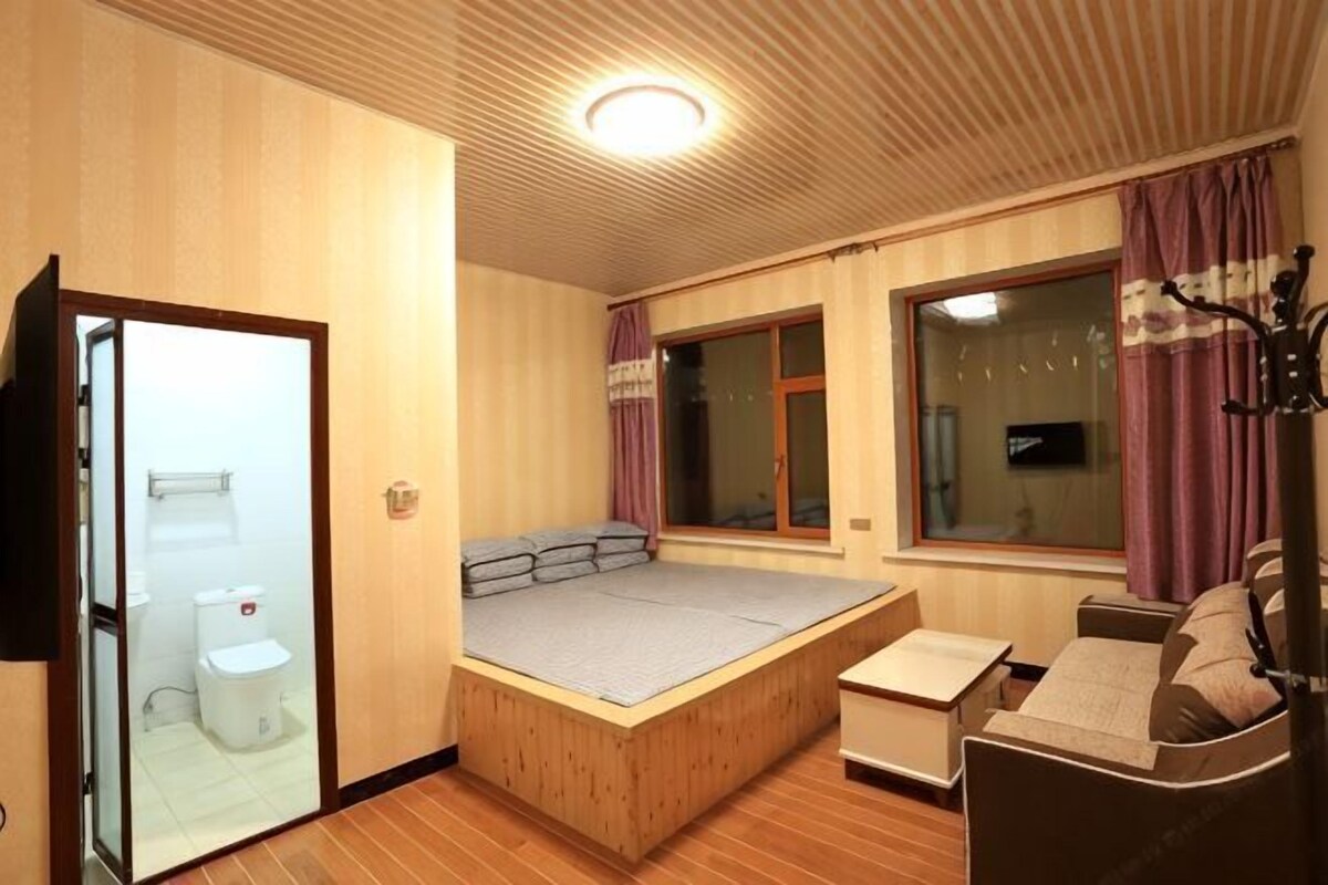 Una habitación con cama, sofá, una mesita, una ventana con cortinas y televisión.