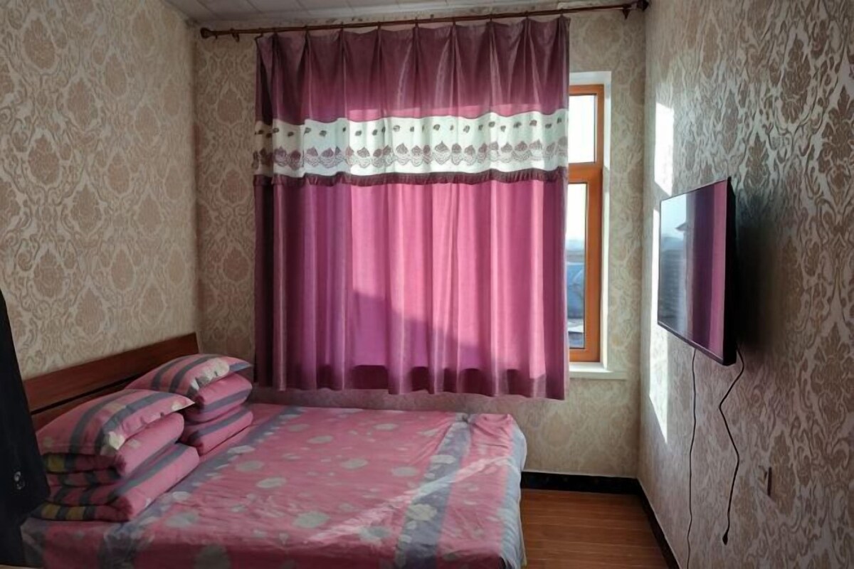 Un dormitorio con cama, cortinas, televisor y ventana.