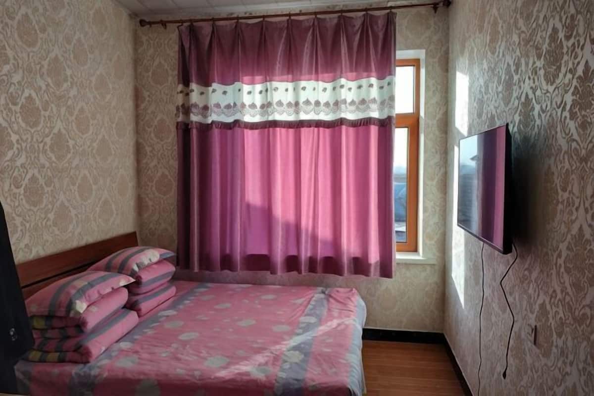 A bedroom with a bed, curtains, a TV, and a window.